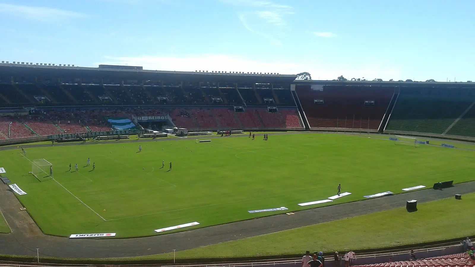 Interior do Estádio Municipal Parque do Sabiá em Uberlândia, com o gramado, as arquibancadas e as cadeiras vermelhas em primeiro plano